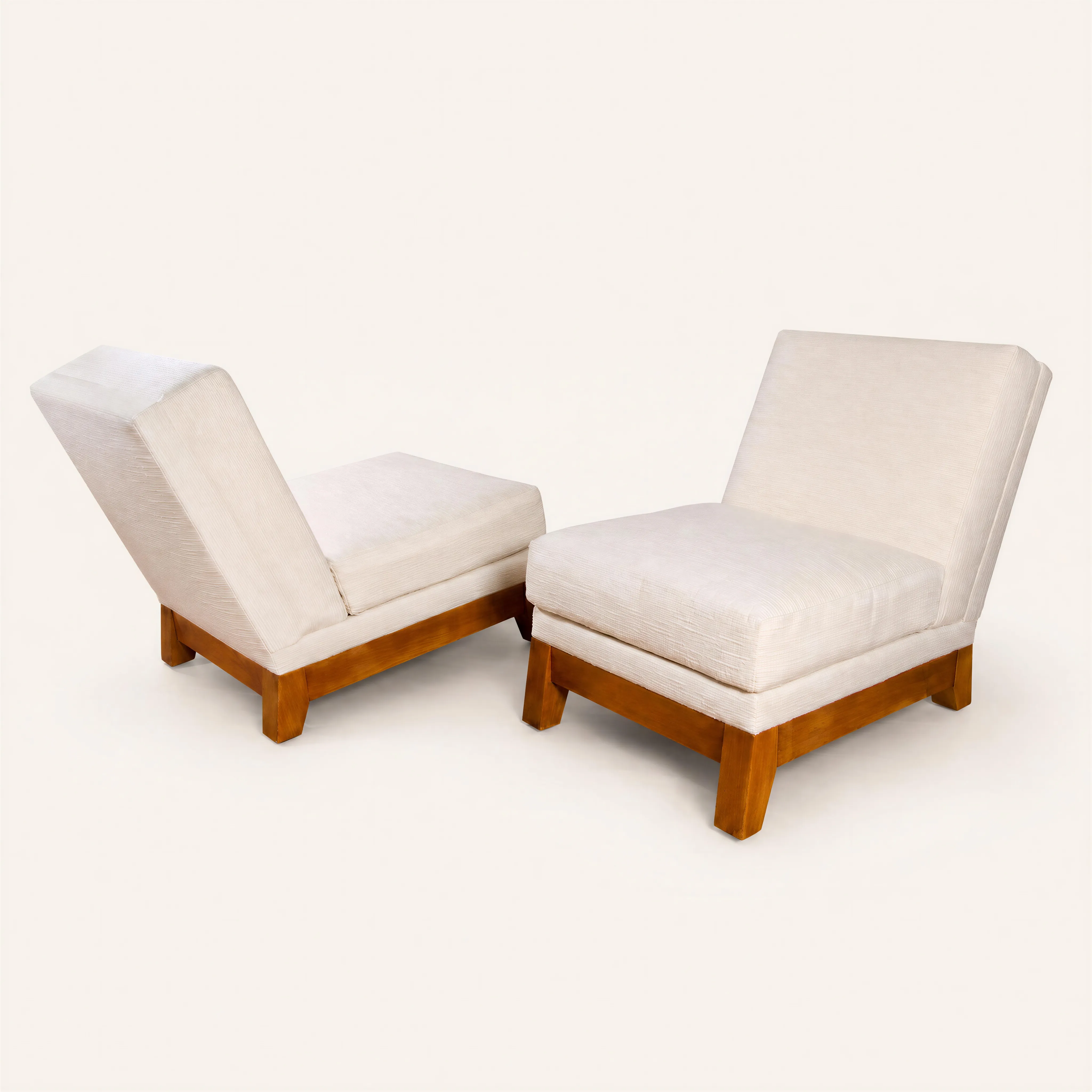 A pair of low, armless lounge chairs reflecting the clean, modernist aesthetic of the 1930s. Each chair features a solid rectangular pearwood base supported by four legs. The deep seat and slanted backrest are thickly padded and upholstered in a light cream fabric. 
Accompanied by a certificate of authenticity from Amélie Marcilhac.