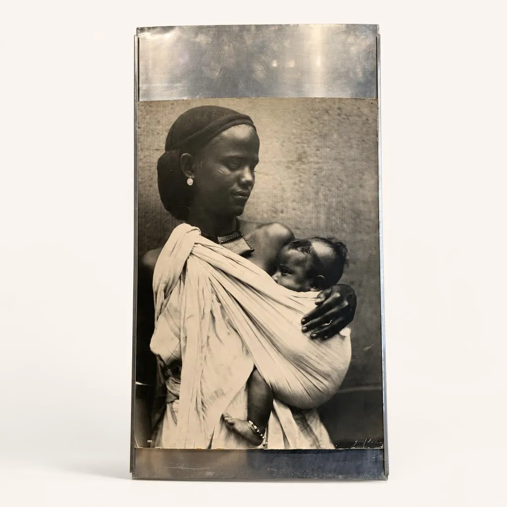 Ce cadre rectangulaire vertical est réalisé en aluminium. Il se distingue par des rebords latéraux délicatement galbés ainsi que de larges bandes métalliques pleines venant encadrer la composition en haut et en bas. 

Il présente un tirage photographique en noir et blanc réalisé par Yola Niclas, figurant une femme éthiopienne portant son enfant. 

L'œuvre porte le monogramme « PEL » du créateur ainsi que les numérotations « 33 » et « 10/1 ».

