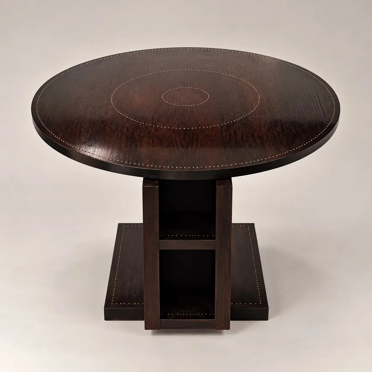 Table basse  à la structure architecturale asymétrique en chêne foncé clouté. L'objet se compose d’un plateau circulaire surmontant un piétement géométrique évidé formant niche de rangement. 

André Sornay développe son premier brevet en 1932 : la technique du «cloutage» qui rappelle les rivets d’avion. Ce procédé permet de réunir des panneaux plaqués d’essences fines à la structure du meuble. L’alignement des clous devient ainsi une marque de fabrique et un élément décoratif. Ce brevet engendre la fabrication de « mobiliers cloutés » diffusés en petite série, et accessibles au plus grand nombre.