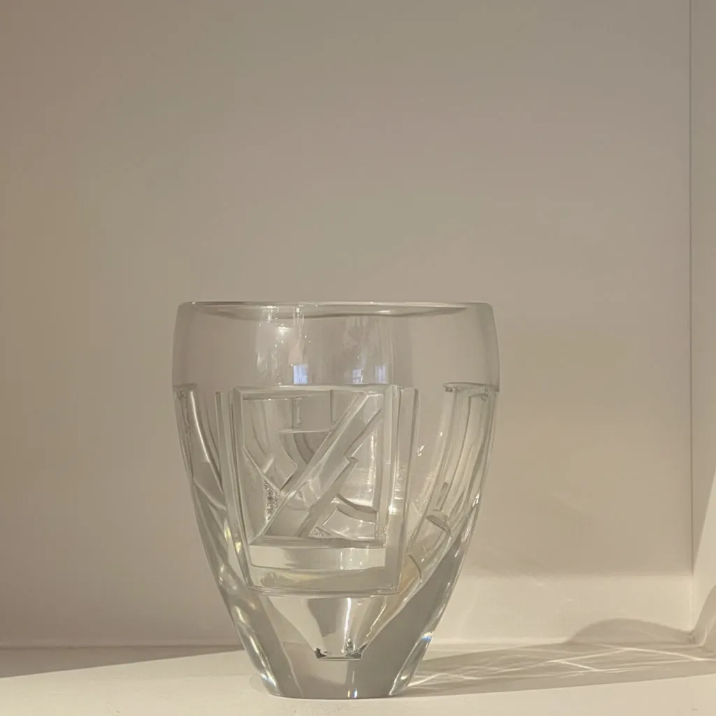 Vase en verre massif transparent. Le corps est sculpté en taille directe de motifs géométriques profondément incisés, associant des registres d'arcs, de cercles et de lignes droites.