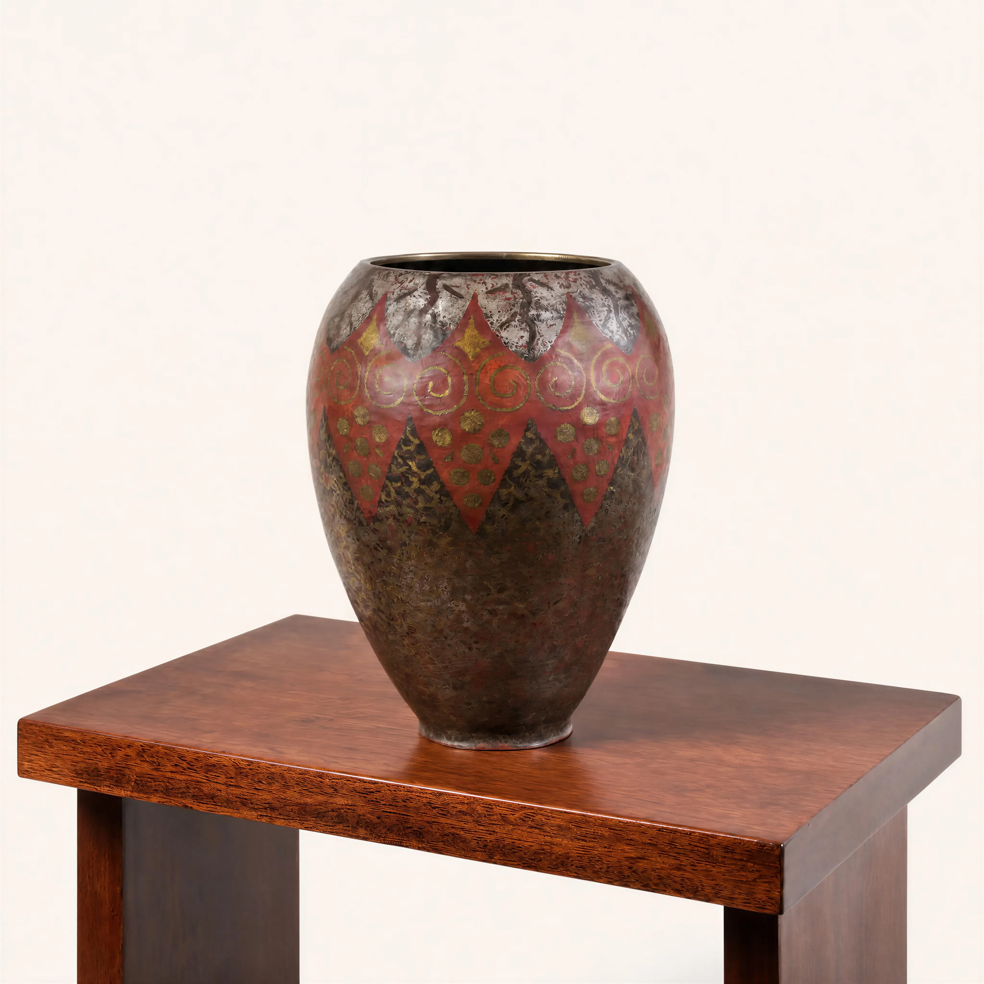 Vase de forme ovoïde en dinanderie à col resserré, témoignant de la parfaite maîtrise des patines par le feu de Claudius Linossier. Le corps du vase présente une riche texture jaspée aux nuances sombres, brunes avec une large frise dentelée rouge brique formant des pointes vers le bas et vers le haut. Cette bande centrale est finement incrustée de motifs géométriques dorés, associant une suite rythmée de volutes et des groupements de pastilles disposées en triangles. La partie supérieure offre une transition vers une patine grise et argentée.
Signé « CL.LINOSSIER »