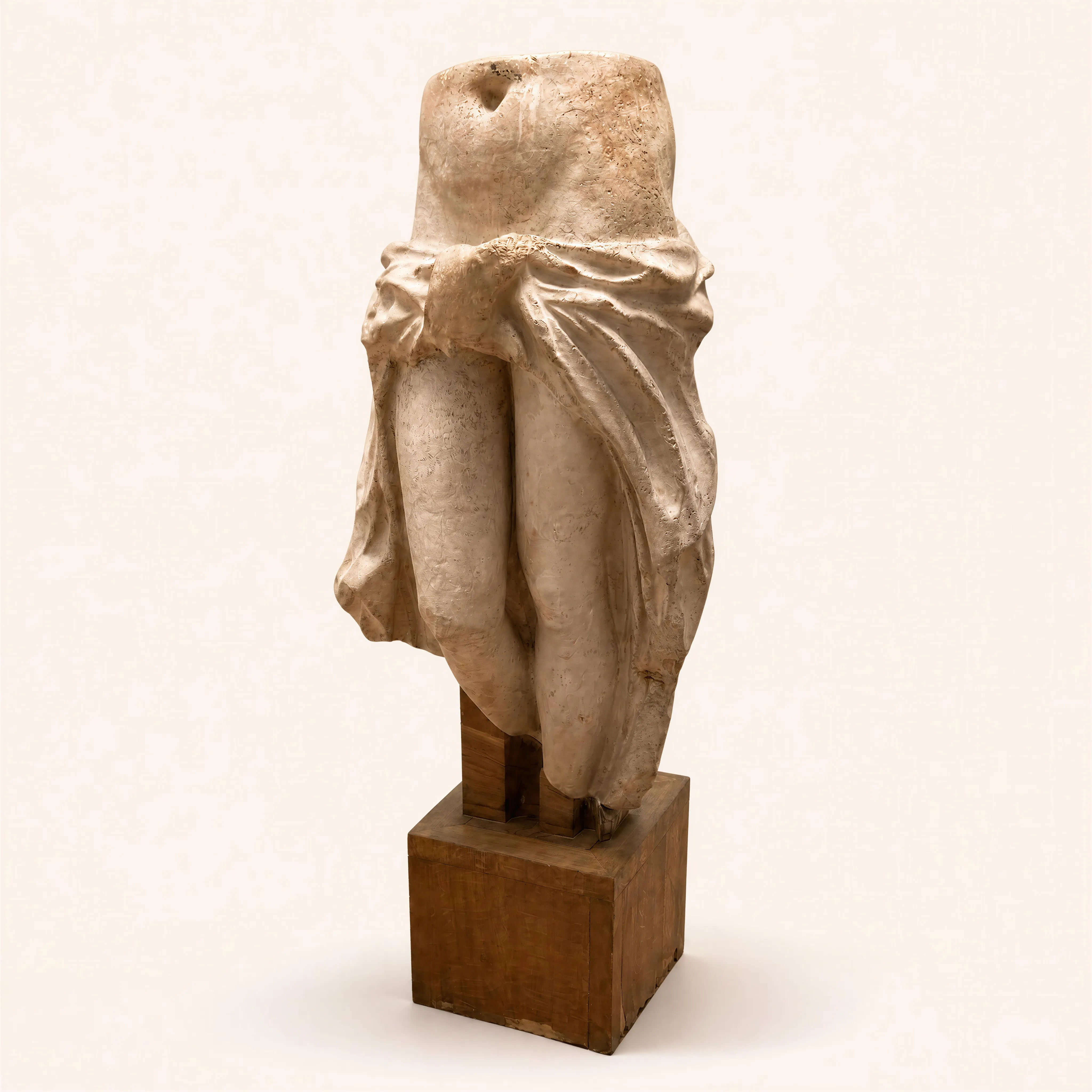 A fragmentary sculpture in the round crafted from chamotte clay, depicting the lower torso of a female figure from the waist to the mid-thighs. The composition is defined by a heavy draped fabric knotted at the front of the hips, with deep folds falling along the sides of the legs. The raw, textured surface of the clay emphasizes both the anatomical modeling and the sculptural volume of the drapery. The piece is mounted on its original, geometric rotating oak base. 
Not signed.