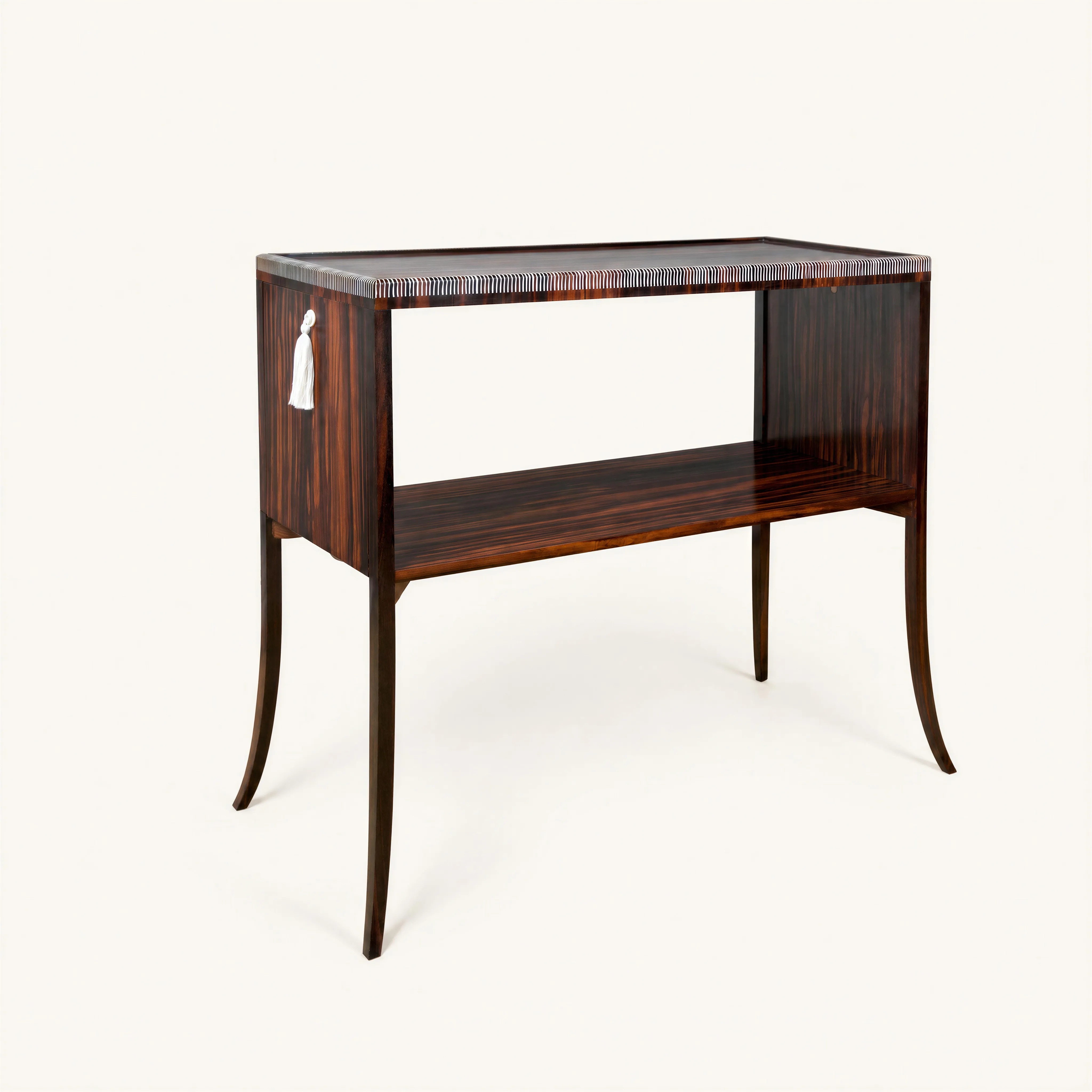 A Macassar ebony drop-leaf sideboard. The rectangular top features a rim highlighted by a remarkably delicate ivory inlay designed to mimic a herringbone passementerie pattern. This top is flanked by two retractable lateral drop leaves, each fitted with a circular ivory pull handle from which a white fabric tassel hangs. The structure is supported by four extremely slender, sinuous, and curved tapered legs. This sideboard also features an open lower shelf with a raised border.
Certificate from Mr. Jean-Marc Maury.