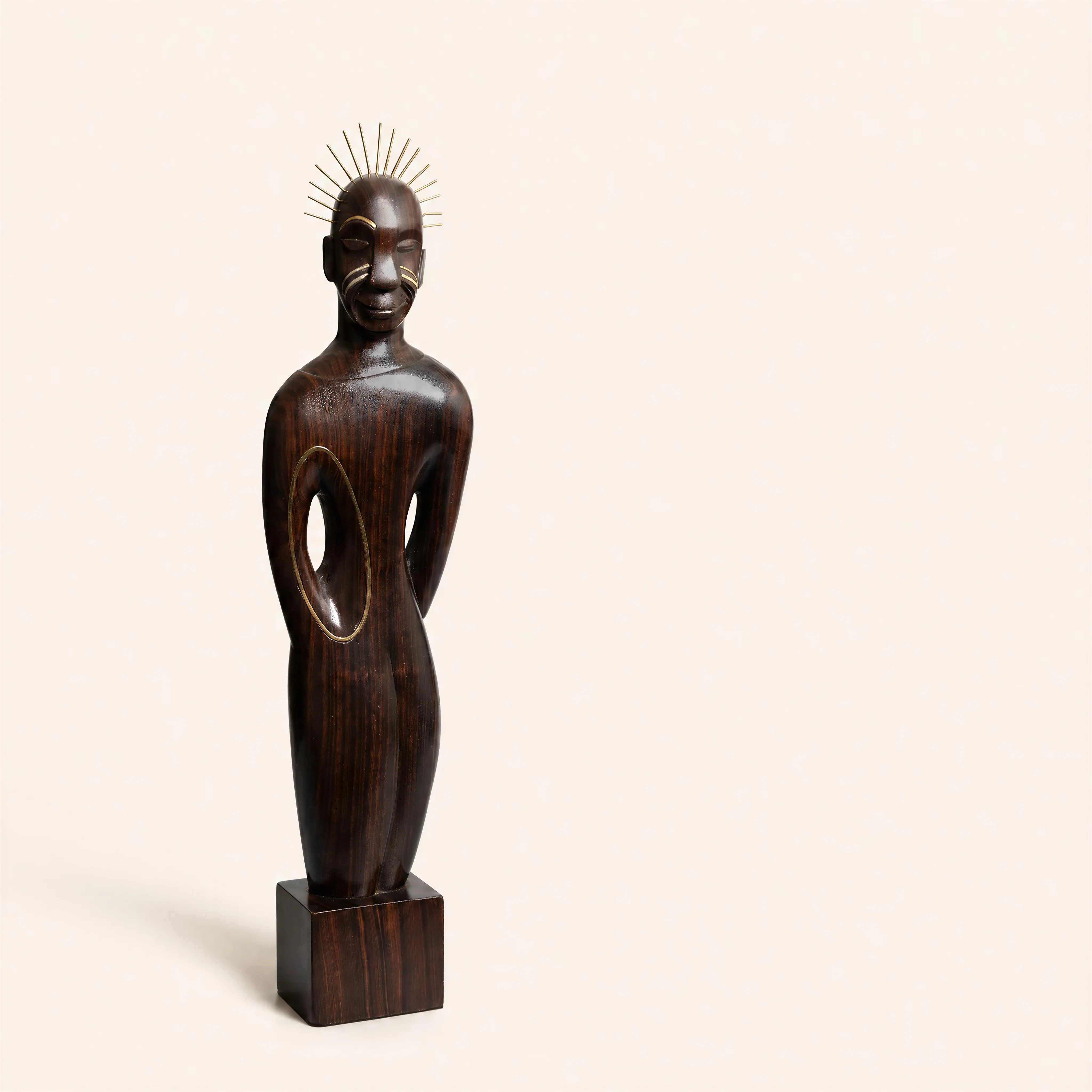 Sculpture anthropomorphe en ébène de Macassar taille directe figurant une silhouette longiligne et stylisée, campée sur son socle d’origine. Les bras s'intègrent de manière fluide dans la masse du buste, ménageant sur le flanc droit un jour ovale ajouré, souligné par un filet de laiton incrusté. Le visage géométrique et hiératique est orné de scarifications en laiton argenté et surmonté d’une coiffe rayonnante composée de fines tiges métalliques. 

