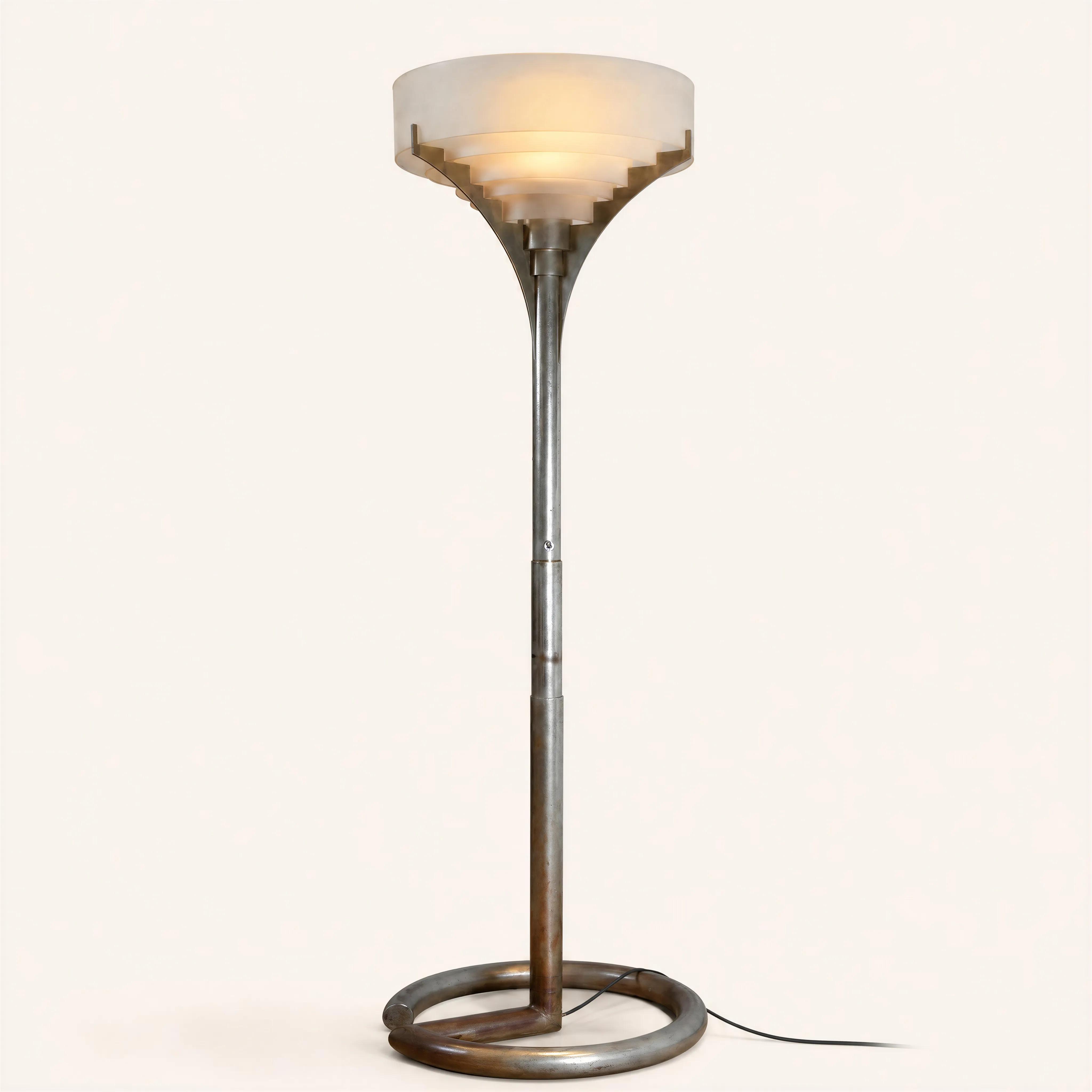 A modernist nickel-plated brass floor lamp resting on a clean, geometric open circular base. The vertical central stem splits and flares at the top into three curved branches designed to cradle the light diffuser. The shade assembly consists of five original concentric frosted glass discs arranged in inverted steps, a hallmark structure of Jean Perzel's design vocabulary engineered to provide a soft, architectural indirect light diffusion.
Featured in “Art et Décoration”, November 1932, page 321.