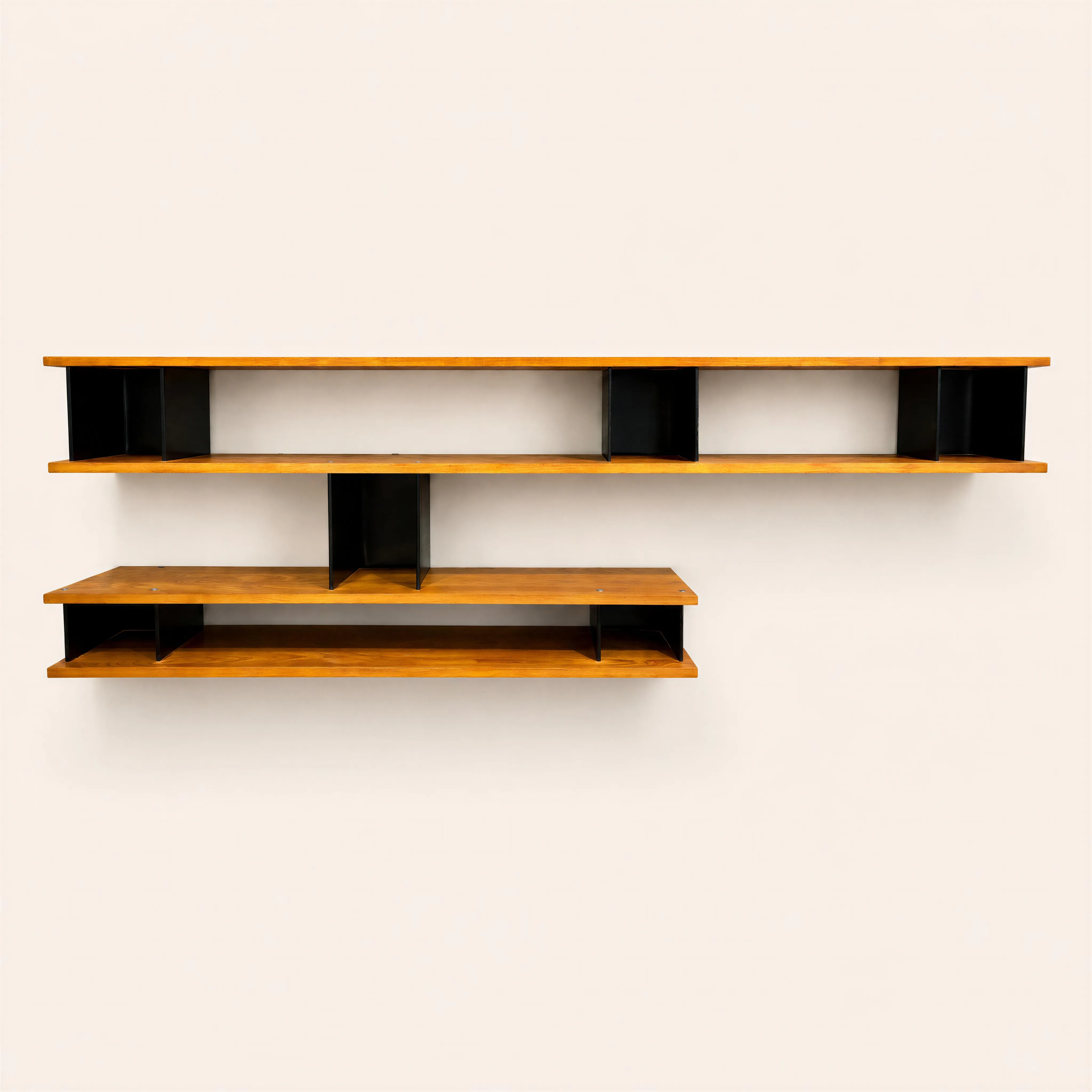 "Nuage" wall-mounted library in ash wood and black lacquered folded sheet metal  featuring a staggered, asymmetrical geometric structure. The 280 cm upper section  consists of two long shelves separated by three open blocks at the ends and center-right, while the shorter lower section is offset to the left with two shelves and two small metal dividers. A single vertical black metal block connects and unifies both tiers. 