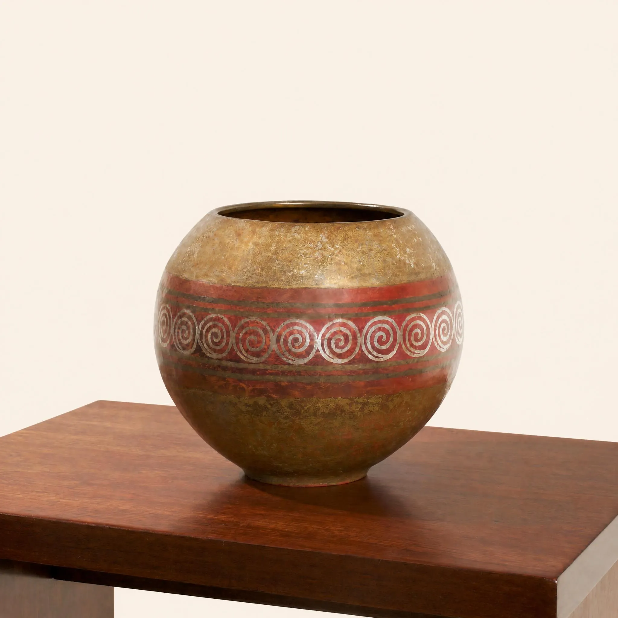 Vase de forme boule en dinanderie à petite ouverture circulaire. La panse est ceinturée en son centre par une large frise horizontale rouge brique, délicatement incrustée d'une suite continue de volutes en spirales d'aspect argenté. Les parties supérieure et inférieure du corps révèlent une patine nuancée aux tonalités dorées, ocres et légèrement ambrées. 
Signé et daté « CL-LINOSSIER 1943 ».