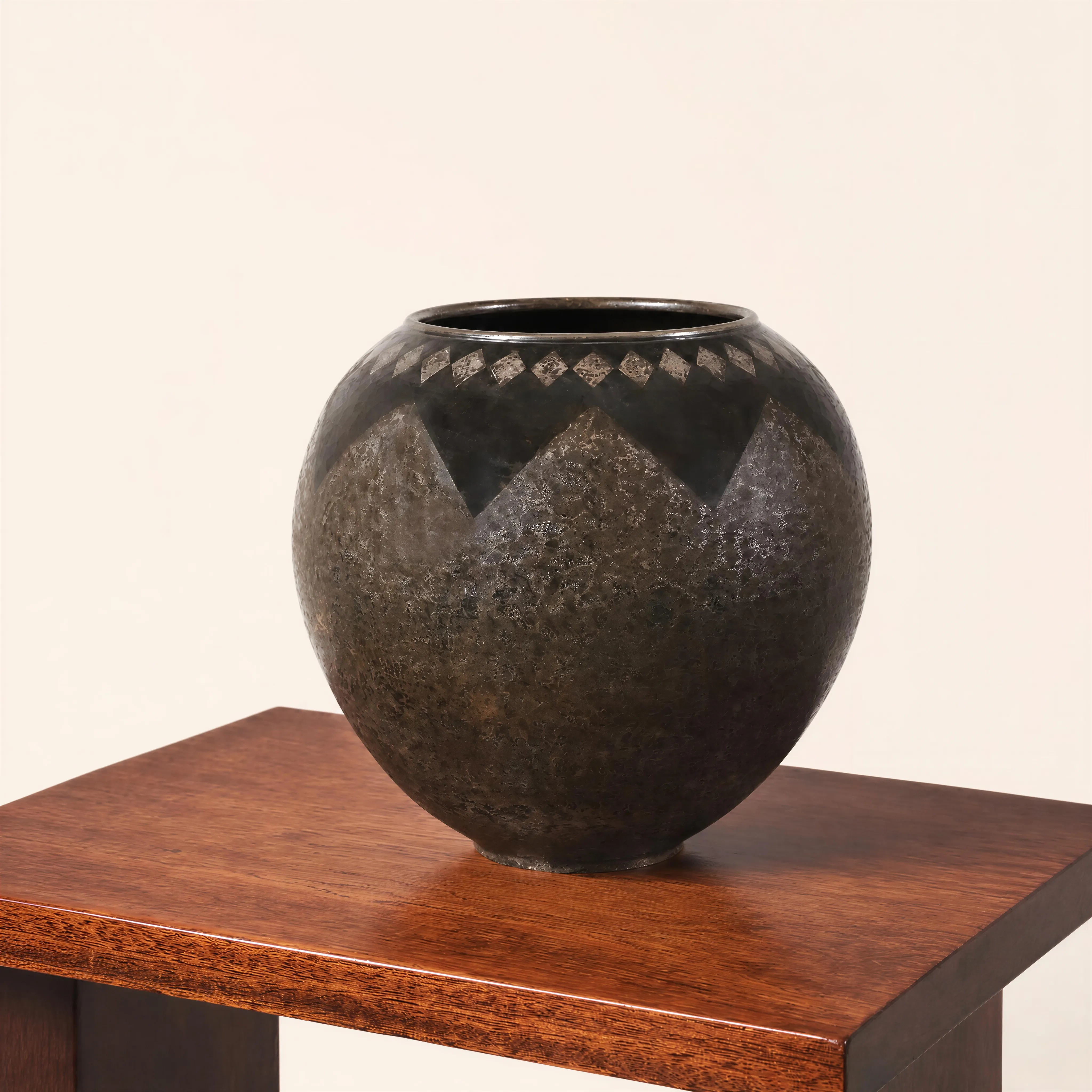 Vase de forme sphérique en dinanderie. La partie centrale est ornée d’un motif géométrique composé de larges pans sombres en pointes se détachant sur une panse à la patine grise et brune finement mouchetée. Le col est quant à lui souligné par une délicate frise de petits losanges aux reflets argentés. L'ensemble des décors et des nuances est obtenu par le travail de la dinanderie, réalisé à partir de feuilles de métal.  
Signé « CL.Linossier ».