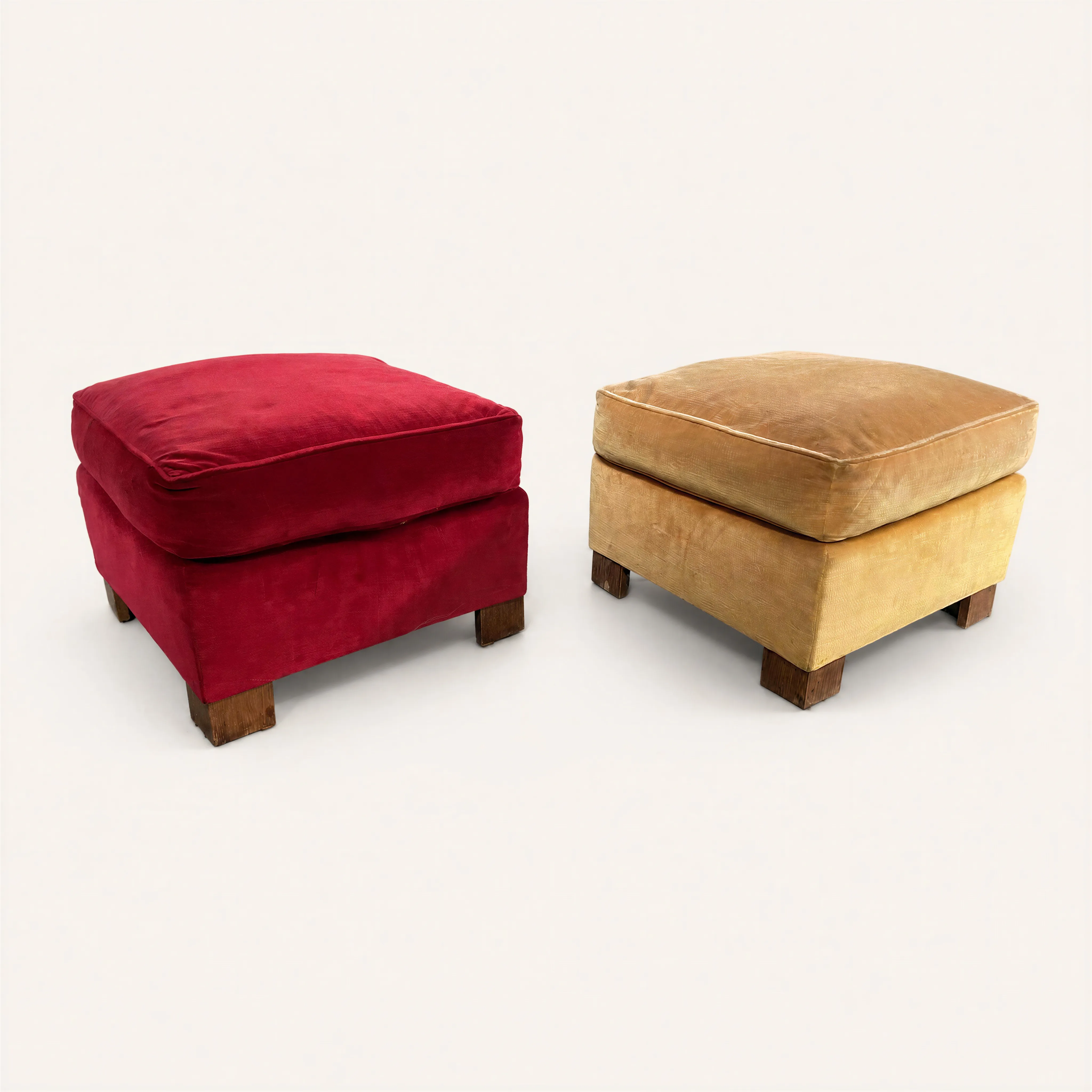 A pair of cubic ottomans attributed to the French designer Jacques Adnet. Each piece features a solid, structured base topped with a thick seat cushion, upholstered in contrasting velvet fabrics: one in deep red and the other in a golden mustard yellow. The ottomans are raised on four sturdy, square-section oak legs, reflecting a modernist geometric rigor. 
Similar model photographed in 1934 within the interiors of Madame Gould's bedroom and Frank Jay Gould's study.