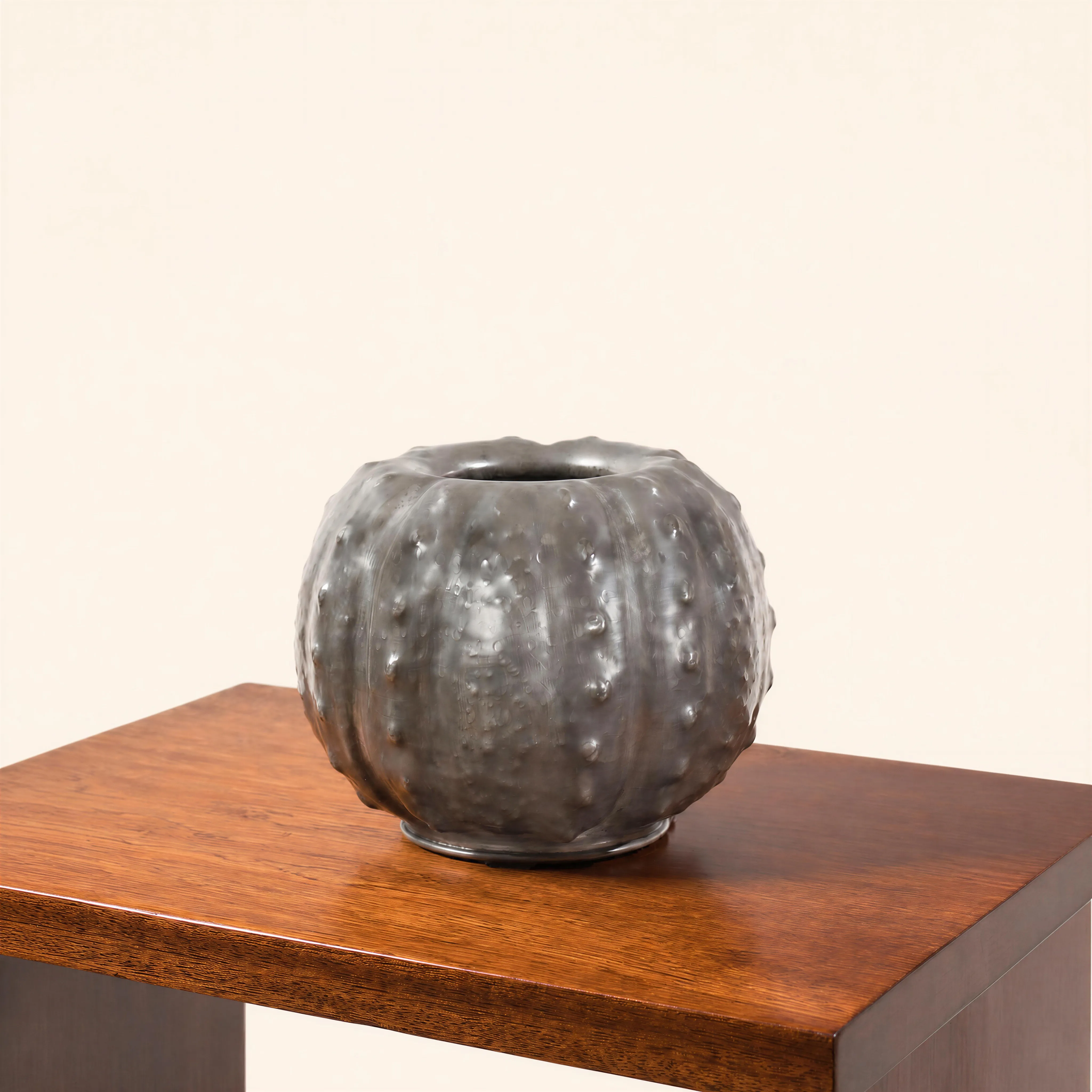 Vase en étain de forme globalement sphérique (vase boule) présentant une petite ouverture circulaire supérieure à bord lisse. La surface en métal repoussé affiche un décor d’inspiration naturaliste évoquant la texture d'un oursin ou d'une forme végétale lobée. Le corps de la pièce est rythmé par des côtes verticales régulières, entièrement recouvertes d'un réseau dense de petites protubérances pointues en relief.
